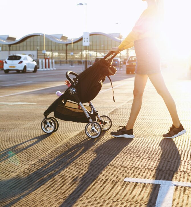 Woman pushing a pram in a car park looking for parent and child parking