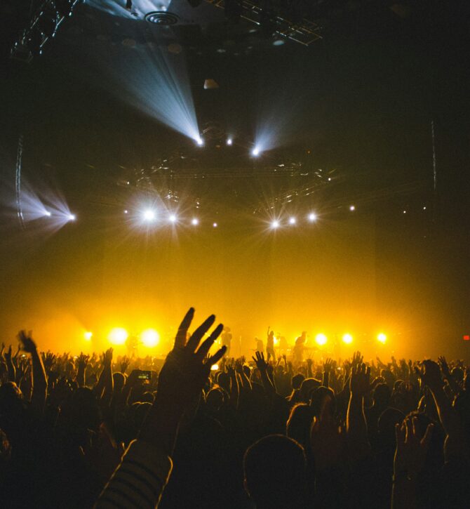 crowd shot at a gig looking toward the stage, peoples hands in the air